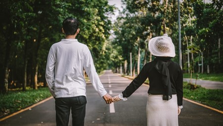 A Heterosexual Couple Holding Hands and Staring at a Road Bracketed by Trees