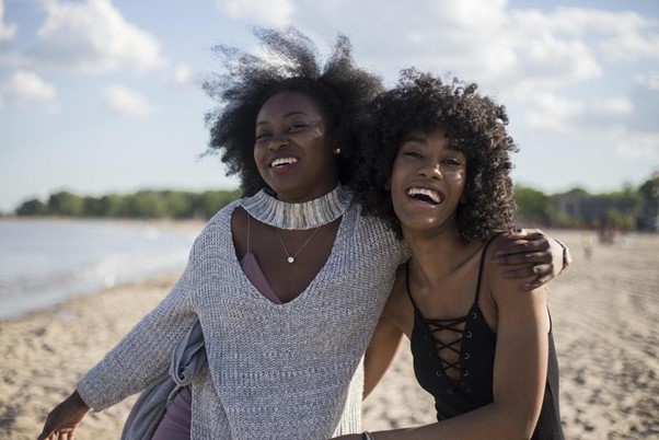 Two Visibly Elated Women Standing Near a Beach Arm in Arm